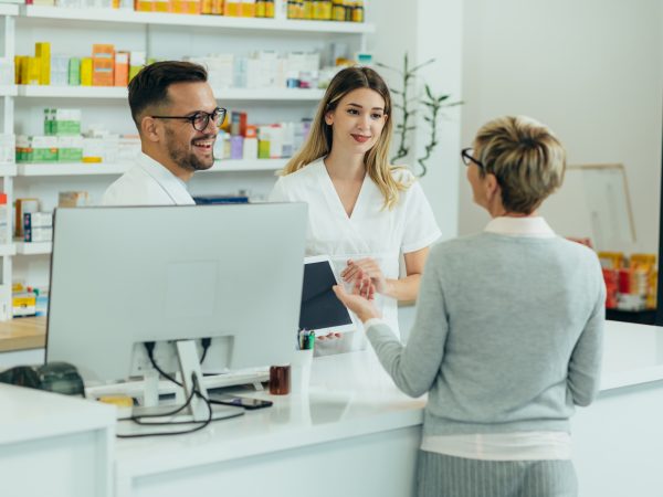 Two pharmacist giving prescription medications to senior female customer in a pharmacy while using digital tablet