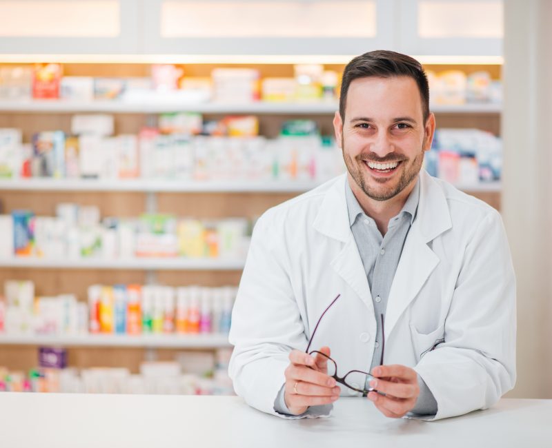 Portrait of a cheerful handsome pharmacist leaning on counter at drugstore.